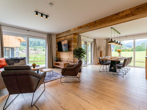 A spacious living area with a wooden ceiling, large windows, a dining table, and comfortable seating. - Luxurious house with sauna close to ski area (Kreischberg)
