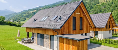 A wooden house with a sloped roof, stone foundation, and a small attached structure.