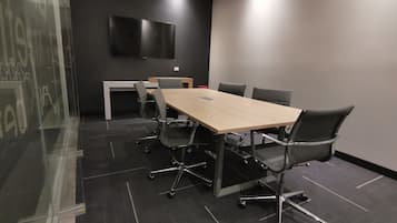 Un salón de conferencias con una larga mesa, seis sillas, un televisor montado en la pared y un separador de vidrio.