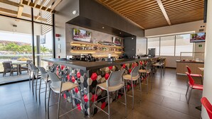 A modern bar area with a wooden ceiling, a bar counter with various bottles, and several bar stools.