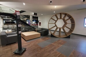 A modern interior with a central wooden wheel structure, grey sofas, and a wooden coffee table. - Ramada Encore by Wyndham Guadalajara Aeropuerto (El Salto)