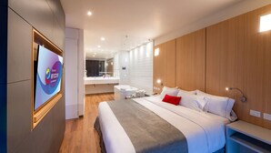 A modern hotel room with a large bed, a bedside table, a TV, a bathroom with a mirror, and wooden paneling on the walls.
