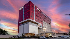 A modern hotel with a prominent red and white facade, multiple floors, and a flat roof design.