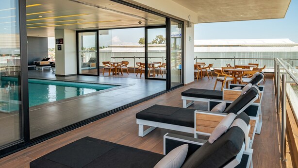 A rooftop pool area with lounge chairs and tables, a swimming pool, and a view of the cityscape.
