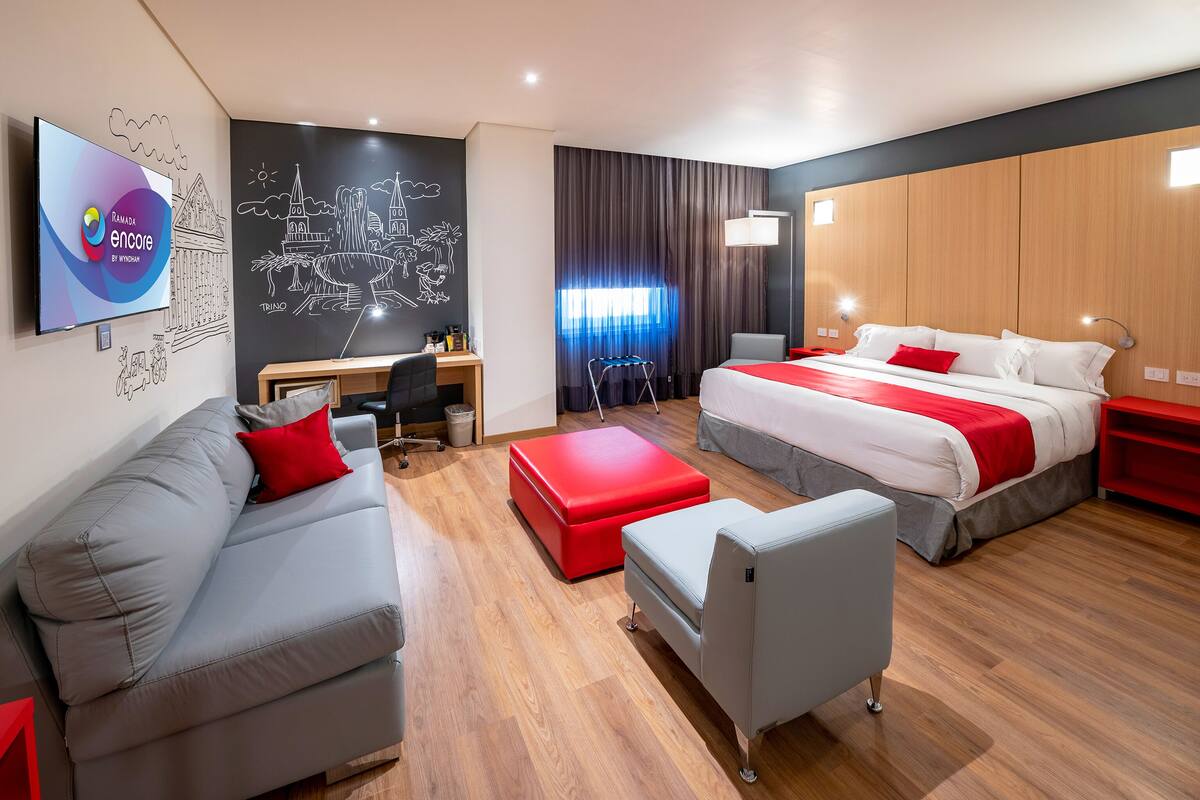 Une chambre d’hôtel moderne équipée d’un grand lit, d’un canapé, d’un bureau et d’un téléviseur affichant le logo de la chaîne Ramada Encore.