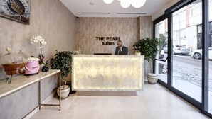 A reception desk with a sign reading "The Pearl Suites," a large window with a city view, and a modern chandelier. - The Pearl Suites (Istanbul)