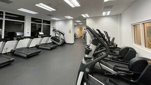 Une salle de sport équipée de plusieurs tapis de course, de vélos d’exercice et d’un mur recouvert de miroirs.