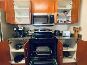 Efficient kitchen with microwave and oven, featuring open shelving and appliances for coffee and toast-making.