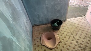 Une petite salle de bain avec des toilettes à la turque, un seau et un sol carrelé.