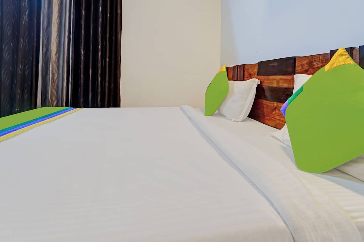 A neatly made bed with white linens, a green pillow, and a wooden headboard.