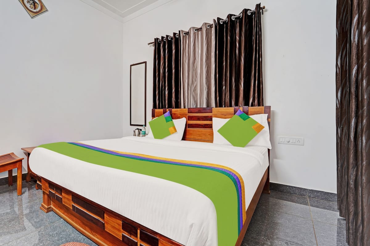 A neatly made bed with a wooden headboard, a chair, and a wall-mounted mirror.