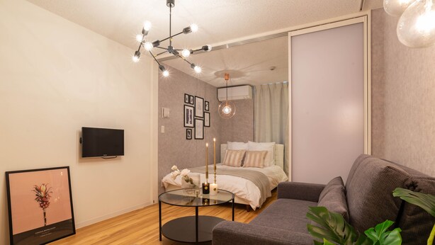 A modern living room with a sofa, a round coffee table, a TV, and a bed with a curtain. - Exia Daikoku AFP Apartment (Osaka)