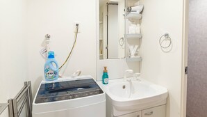 A bathroom with a white sink, a mirror, a towel rack, and a built-in washing machine. - Exia Daikoku AFP Apartment (Osaka)