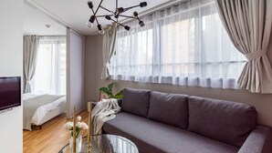 A modern living room with a grey sofa, a glass coffee table, and a TV on the left.