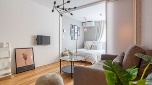 A modern living room with a sofa, a round coffee table, a TV, and a bed with a white headboard.