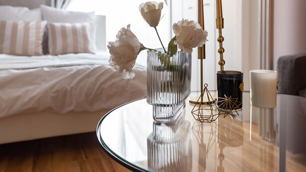 A bedroom with a bed, a bedside table with a vase of flowers, a lamp, and a candle.