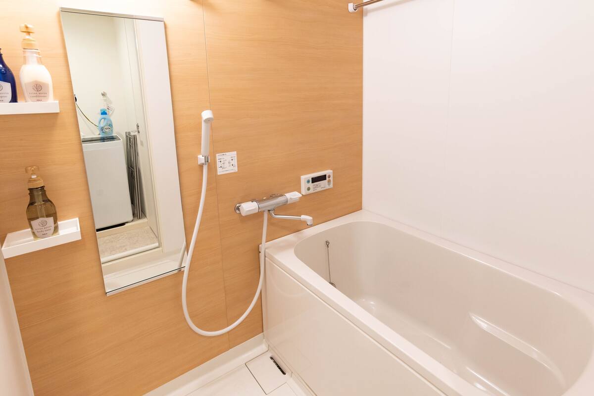 A modern bathroom with a white bathtub, a handheld showerhead, a mirror, and a shelf with toiletries.