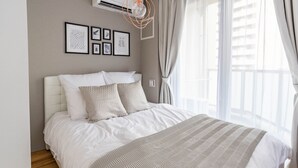 A neatly made bed with a striped blanket, a headboard, and a series of framed pictures on the wall. - Exia Daikoku AFP Apartment (Osaka)