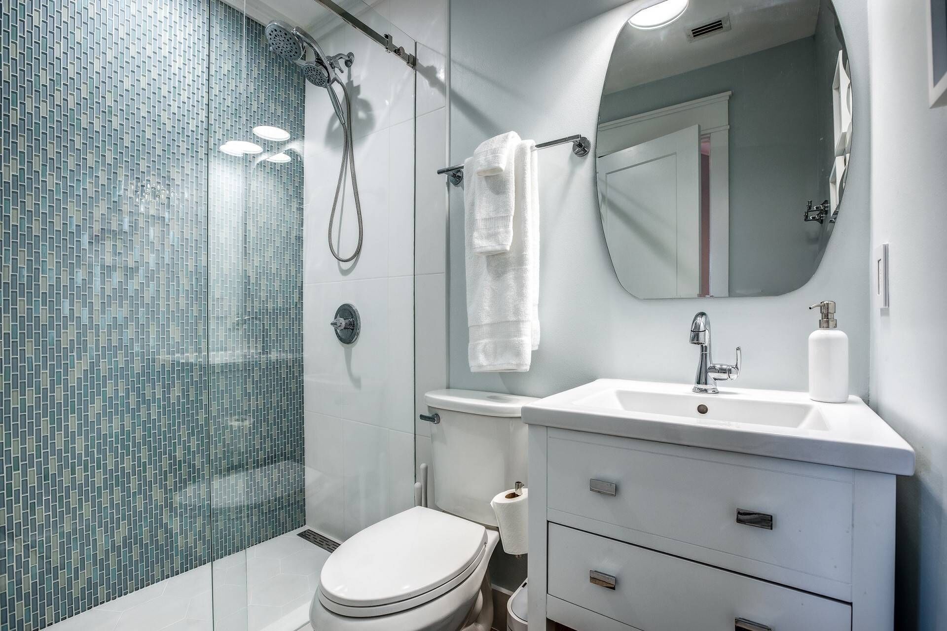 Une salle de bain moderne avec une douche à parois de verre, des toilettes blanches, un lavabo avec un miroir et un meuble-lavabo avec des tiroirs.