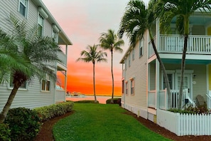 A beachfront property with a well-maintained lawn, palm trees, and a view of the ocean at sunset.