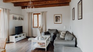 A modern living room with a wooden ceiling, a white entertainment unit, a grey sofa, and a glass coffee table. - Casa al Tanaro | Spacious country house with pool in southern Piedmont (Castellino Tanaro)