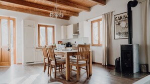A spacious kitchen with wooden cabinets, a dining table with chairs, a chandelier, and a black stove. - Casa al Tanaro | Spacious country house with pool in southern Piedmont (Castellino Tanaro)