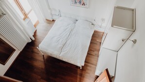 A bedroom with a white bed, wooden flooring, a white radiator, and a framed picture on the wall. - Casa al Tanaro | Spacious country house with pool in southern Piedmont (Castellino Tanaro)