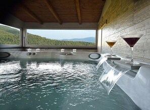 A hot tub with a view of a mountainous landscape, two glasses of wine, and a wooden ceiling.
