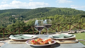 A table set with plates of food and two wine glasses, overlooking a forested hillside. - Villa Sonia M: A characteristic and welcoming cottage located in an isolated position, on the slopes of a hill which is covered with olive groves, with Free WI-FI. (Gualdo Cattaneo)
