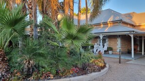 Een gebouw met een overdekte patio, omringd door weelderige begroeiing, waaronder palmbomen en diverse planten.