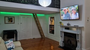 Een woonkamer met een houten vloer, een witte bank, een open haard en een aan de muur bevestigde televisie.