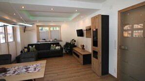A modern living room with a sofa, a dining table, and a TV mounted on the wall. - Haus Goldmann by Interhome (Ginzling)