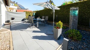 Eine Terrasse im Freien mit Tisch, Stühlen, einem Grill und einem dekorativen Zaun.
