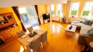 Ein modernes Wohnzimmer mit Holzboden, einem Essbereich mit Tisch für vier Personen, einem Sofa und einem Fernseher.
