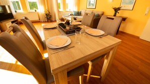 Ein Essbereich mit einem Holztisch, gedeckt für vier Personen, Stühlen und einem Fernseher im Hintergrund.