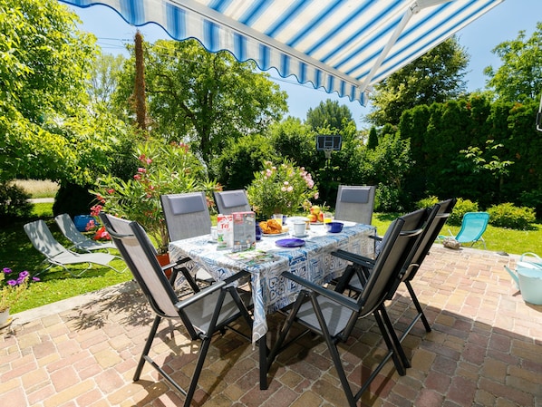 Une terrasse extérieure avec une table dressée pour quatre personnes, entourée de chaises, et protégée par un auvent à rayures.