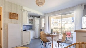 A spacious kitchen with white cabinets, a dining area with wicker chairs, and a balcony with a view. - Montaigu by Interhome (Cabourg)