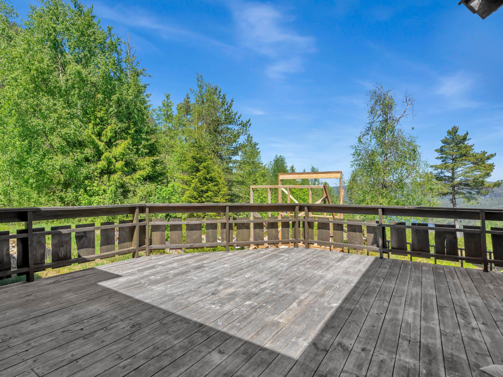 A wooden deck with a railing, surrounded by trees and a clear sky.