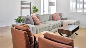 Una sala moderna con un sofá seccional gris, dos sillones de cuero, una mesa de centro de madera y una mesita auxiliar con un globo terráqueo y una planta.