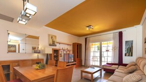 A spacious living area with a wooden dining table, red cushioned chairs, a beige sofa, and a red armchair. There is a bookshelf, a flat-screen TV, and a painting on the wall. - Vacation home Ni Hao by Interhome (Calpe/Calp)