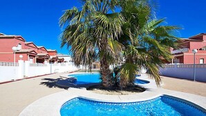 A swimming pool with a palm tree in the center, surrounded by a white fence and red buildings. - Vacation home Ni Hao by Interhome (Calpe/Calp)