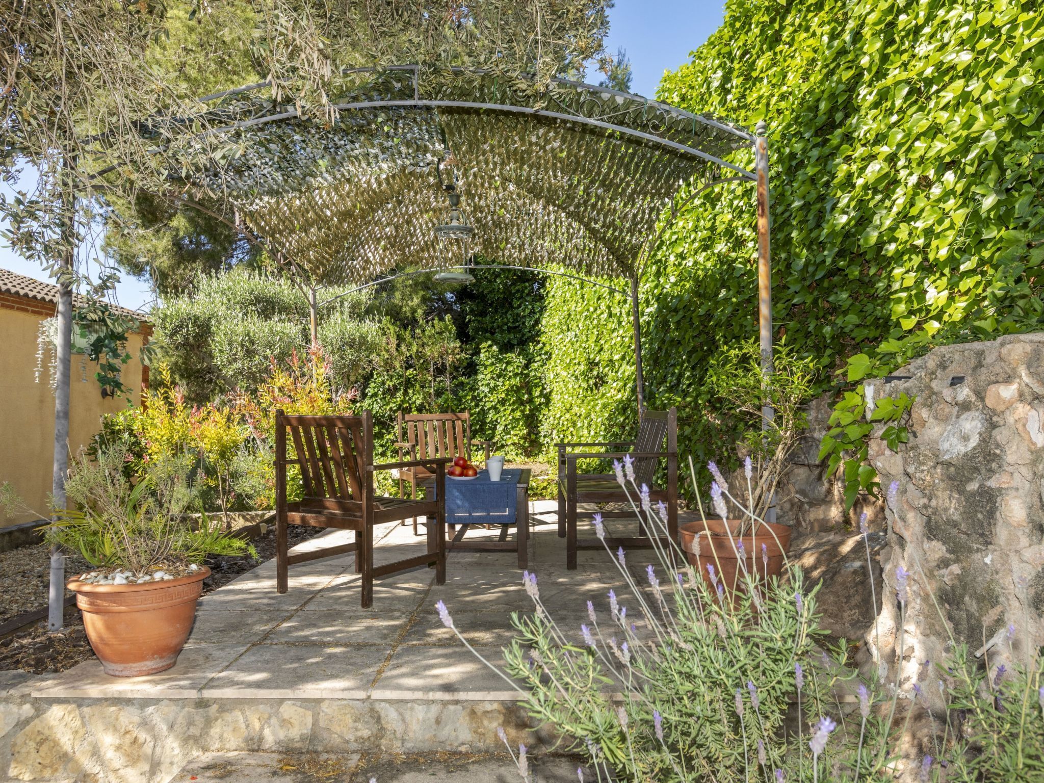 An outdoor patio with wooden furniture, a pergola, and potted plants.