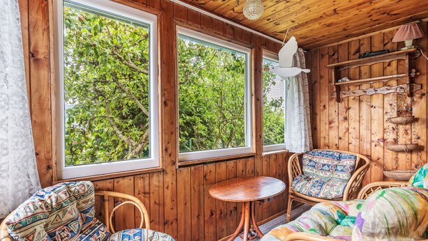 A cozy room with wooden walls and large windows, wicker furniture, and a hanging lamp. - Vacation home Vesec by Interhome (Liberec)