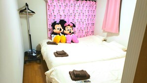 A hotel room with two beds, a pink Mickey Mouse-themed curtain, and Mickey Mouse plush toys on the beds. - Vacation Rental Maihama (Urayasu)