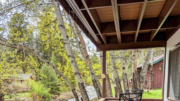 A wooden deck with a table and chairs, overlooking a river and forest. - Rocky Mountain Riverside Escape; 1 Mile to Park (Estes Park)