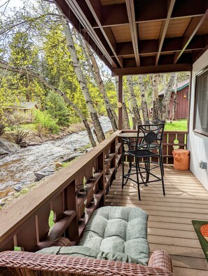 Een houten terras met een tafel en stoelen, met uitzicht op een rivier en bos.