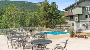 A pool area with outdoor seating, a building with a balcony, and a mountainous backdrop. - Rocky Mountain Riverside Escape; 1 Mile to Park (Estes Park)
