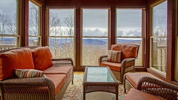 Un solárium con mobiliario de mimbre, amplias ventanas y vistas a un paisaje montañoso.