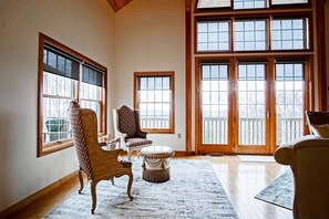 Une pièce spacieuse avec de grandes fenêtres, un plancher en bois et différents types de sièges, notamment un fauteuil et un canapé.