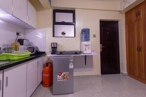 A compact kitchen with white cabinets, a small refrigerator, a water dispenser, and a coffee machine. - Stay.Plus Kileleshwa Executive Studio (Nairobi)